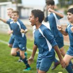 Energetic preteen and teenage male footballers cheering and punching the air as they run onto field for training session.