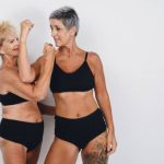 caucasian mother and daughter with tanned skin and short hair, in black underwear, posing together showing strength and determination together, in studio with white background.