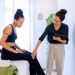 Therapist assisting client with knee pains in massage therapy room.