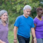 A small group of adults are seen walking together as they work to stay fit and active.  They are each dressed comfortably and appear happy as thy talk amongst each other while taking their fitness outdoors.